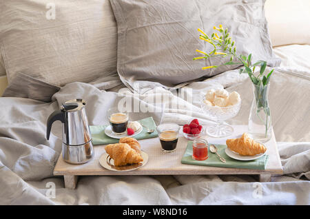 Romantic Breakfast  or brunch for two in bed. Coffee maker  and coffee glasses, croissants, jam, berries, meringue and flowers on wood tray. Romantic Stock Photo