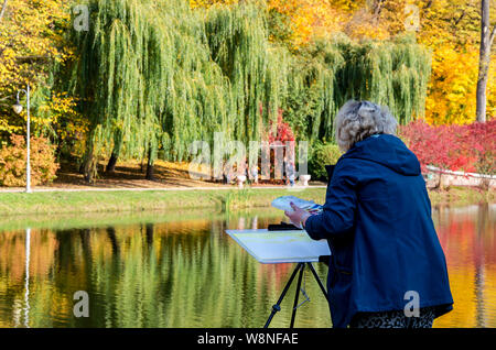 an elderly woman paints a picture looking at a bright autumn landscape on a sunny day in the park Stock Photo