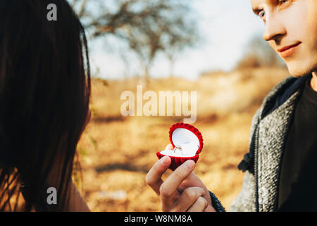 Crop handsome guy holding box with elegant engagement ring while proposing to unrecognizable female on sunny day in nature Stock Photo