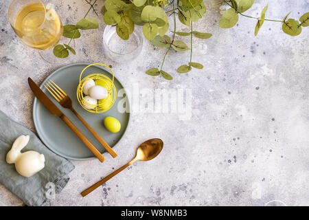 Happy Easter concept. Top view of beautiful spring table settings, plate with gold cutlery, easter bunny and eggs with and green. Copy space. Stock Photo