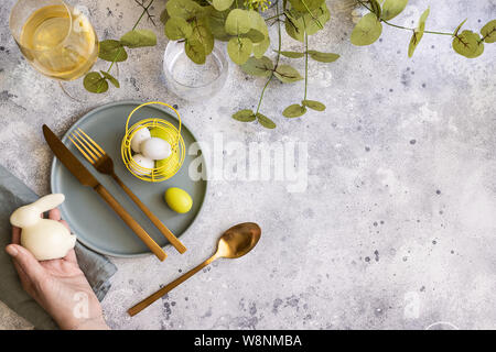 Happy Easter table setting:  mint green plate with  gold cutlery and  woman hand with bunny, painted Egg and wine. Scandinavian style  background with Stock Photo