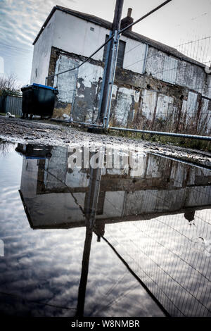Derelict and empty houses behind a fence, reflected in a pool of water near Consett, County Durham, England, UK Stock Photo