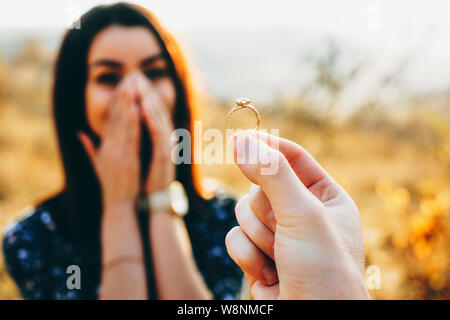 Hand of anonymous man holding elegant engagement ring while proposing to amazed lady on sunny day in countryside Stock Photo