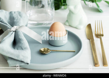 Happy Easter  table setting with traditional  Easter decoration :  white bunny,  natural egg in mint green plate with  gold cutlery. Scandinavian styl Stock Photo