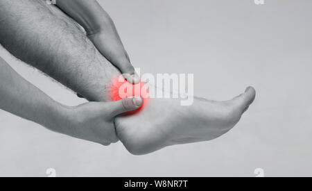 Man holding his ankle in pain, monochrome photo Stock Photo