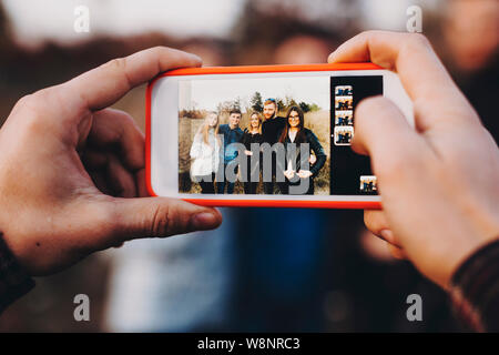 Closeup shot of hands of unrecognizable man using modern smartphone to take photo of group of young friends in amazing countryside Stock Photo
