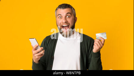 Emotional man holding credit card and smartphone Stock Photo