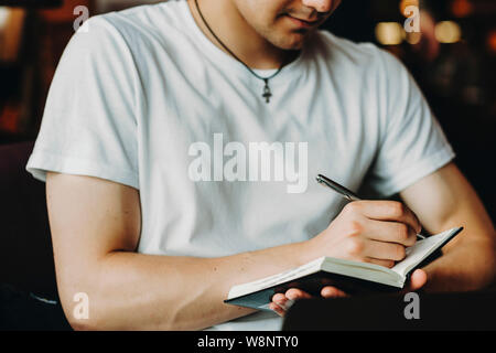 Crop young man taking notes with pen in small notepad Stock Photo