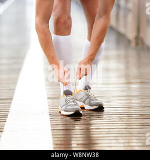 Running shoes. Man tying shoe laces. Closeup of male sport fitness runner getting ready for jogging workout outdoors path in rain in urban city setting. Stock Photo
