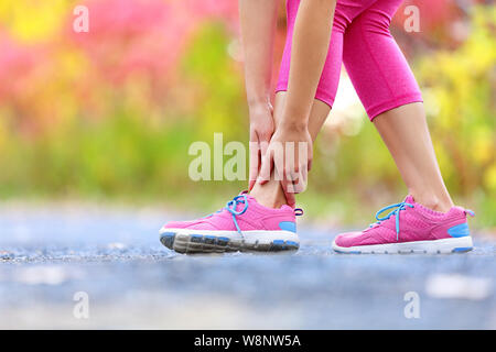 Running sport injury - twisted broken ankle. Female athlete runner touching foot in pain due to sprained ankle. Stock Photo