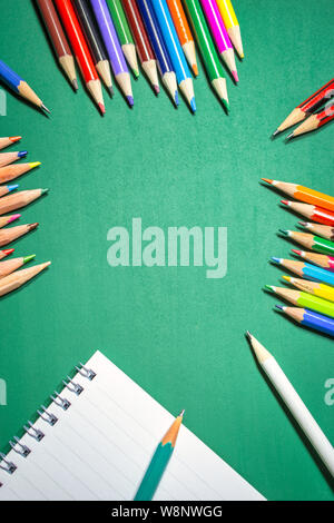 Blank paper and colorful pencils over green chalkboard, back to school concept. Top view with copy space. Stock Photo