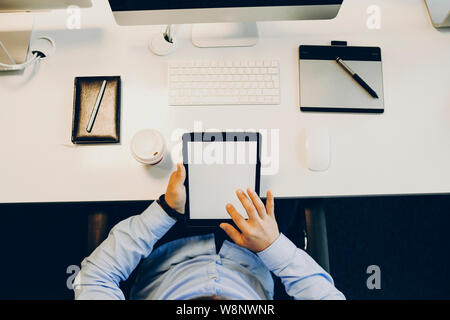 From above shot of anonymous guy sitting at office table and browsing modern tablet with blank screen.Crop office working browsing tablet Stock Photo