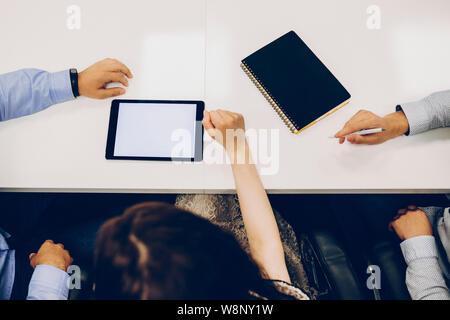 From above shot of crop people with notebook and tablet with blank screen sitting at table in office.Anonymous colleagues with tablet and notebook Stock Photo