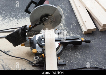The saw stands on a concrete floor with a block of wood prepared for cutting, and already sawn blanks lie nearby Stock Photo