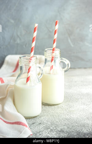 Milk in vintage bottles with stripped red and white straws on grey concrete  table with copyspace Stock Photo
