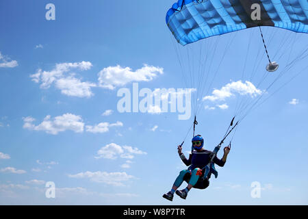 Skydiver under a blue little canopy of a parachute is flies, close-up. High-speed landing of a parachuter against the background of clouds.  USA, Mich Stock Photo