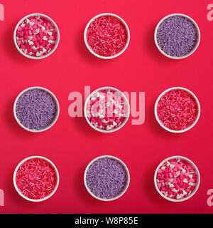 Colorful sprinkles in paper cake molds as pattern  on a pink background. Top view of cake decoration Stock Photo
