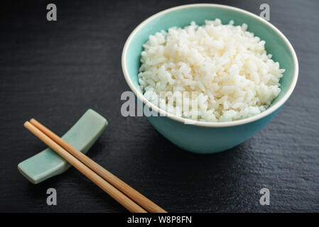 Boiled rice in bowl and  bamboo chopsticks on black slate background closeup Stock Photo