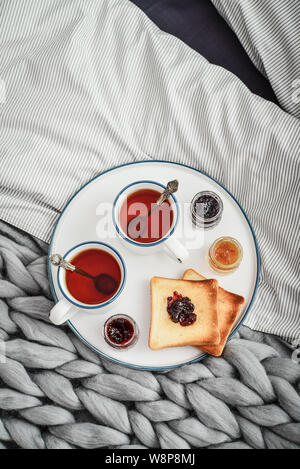 Tray with two cups of black  tea, different jam in jars and toasts on bed at breakfast time, top view Stock Photo