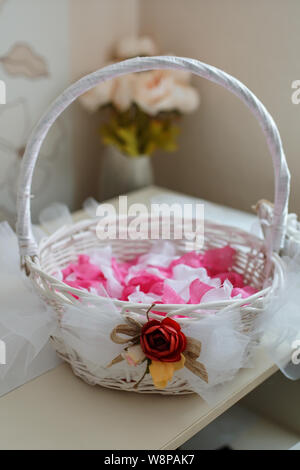 White straw basket with rose petals and  wedding accessories and other gifts on the table. Wedding concept Stock Photo
