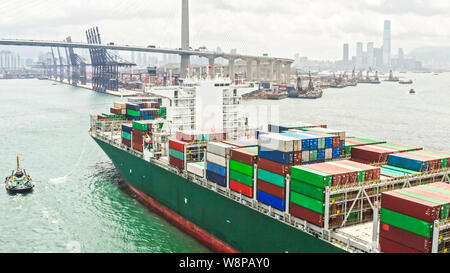 Large cargo ship transporting shipment container arriving Hong Kong port, bridge and city background drone aerial view. Freight transportation concept Stock Photo
