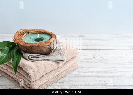 Candle in coconut shell on stack of towels on light background. Spa concept. Stock Photo