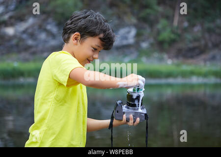 Smiling white bully boy is holding digital camera in his hands and washing it by foam in the countryside. Stock Photo
