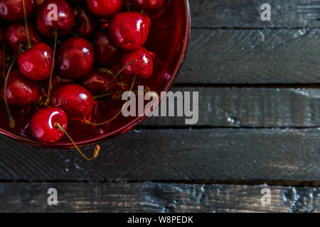 Fresh, ripe cherries in a red glass bowl on black wooden board table background . View from above with copy space Stock Photo