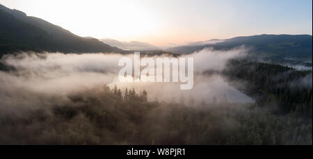 Aerial Panoramic View of Fairy Lake covered in clouds during a vibrant summer sunrise. Taken near Port Renfrew, Vancouver Island, British Columbia, Ca Stock Photo