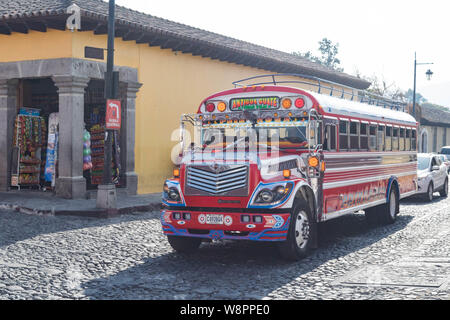 A decorative chicken bus on a cobblestone street and an old yellow buildings, in Antigua, Guatemala Stock Photo