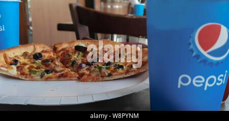 JANUARY 3, 2019-Dubai UAE : Pepsi paper cup with the pepsi logo in front of a cooked pizza. Stock Photo