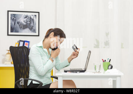 Businesswoman doing online shopping with credit card and talking on mobile phone Stock Photo