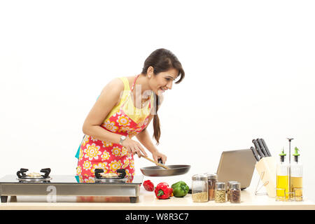 Young woman cooking food in frying pan and looking recipe in laptop Stock Photo
