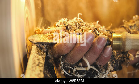 Carpenter handles wood by lathe. Builder works with the workpiece in the workshop. Making beautiful wooden handmade dish. Production of unusual plate. Stock Photo