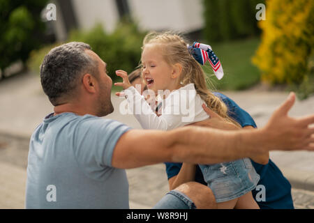 Cute blonde girl making funny face while hugging parents Stock Photo