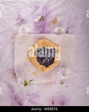 Summer sweet pie cake galette with  blueberry over on white colored fabric background with flowers. Top view Stock Photo