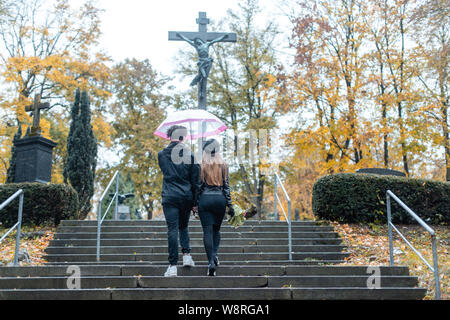 Man and woman walking up steps on cemetery towards a cross Stock Photo