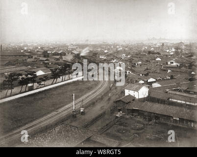 [ 1880s Japan - Railway Tracks in Southern Osaka ] —   Railway tracks of Hankai Tetsudo winding through southern Osaka. Started in 1885 (Meiji 18), the railroad connected Osaka with Sakai. In 1898 (Meiji 22) the company merged with Nankai Railway; it is now known as Nankai Electric Railway. Below the overpass, the railroad crossing can be seen. At this time, trains still stopped at crossings. Beyond the overpass is Nanba Railway Station. Shot between 1886 and 1890.  19th century vintage albumen photograph. Stock Photo