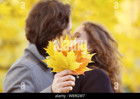 love, relationship, family and people concept - couple with maple leaves kissing in autumn park Stock Photo