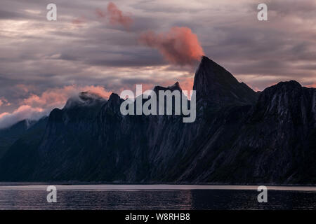Impressive mountain range of Segla over a fjord at midnight under cloudy colorful sky, Senja, Norway