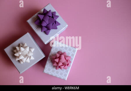 Three light gray gift boxes with colorful bows on pink background. Festive concept. Flat lay. Stock Photo