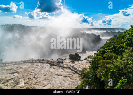 Tourists walking on the footbridge over the Iguazu River in front of the beautiful Iguazu Falls at Brazil side