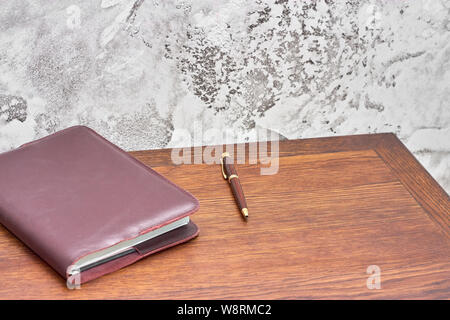Organizer with pen on the wood top table in front of cement wall. Gray loft style wall use for background. Stock Photo