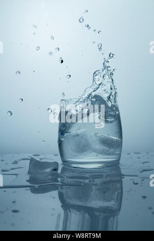 High splash with splashes of pure cold water. Ice falls into a clear drinking glass Stock Photo