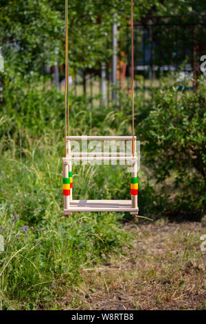 Children's wooden swing on the ropes hang on the background of park greenery, vertical no people Stock Photo