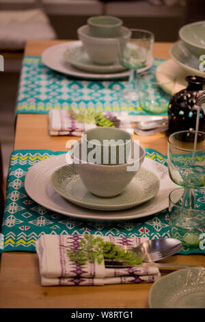 Festive table setting in white and green tones. Plates wine glasses on ethnic napkin with ornament. Beautifully laid table, waiting for guests, tablew Stock Photo