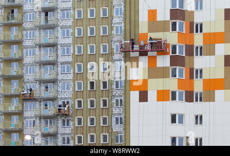 The facade decoration of a residential high-rise apartment building. Workers complete the decoration of the facade. Builders work in a basket on the w Stock Photo
