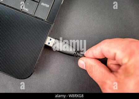 male hand connecting usb cable to laptop closeup overhead view on dark background Stock Photo