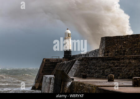 Ocean waves breaking over a harbour wall next to a lighthouse on a stormy day (Porthcawl, Wales, UK)