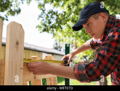 Man uses a tape measure to mark the length of a piece of lumber. Stock Photo
